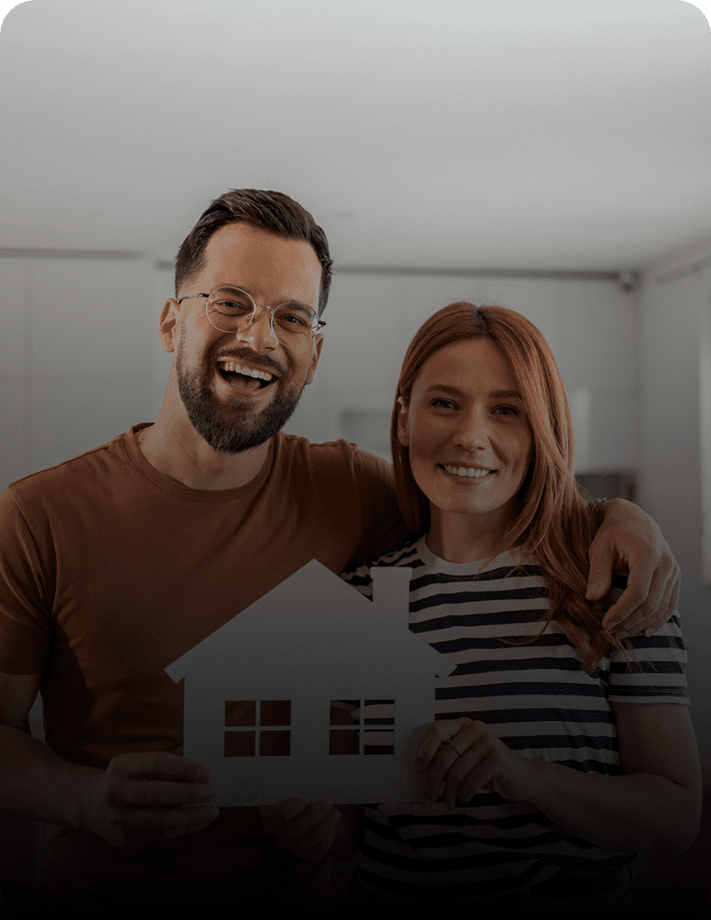 Couple holding house cutout, smiling indoors.